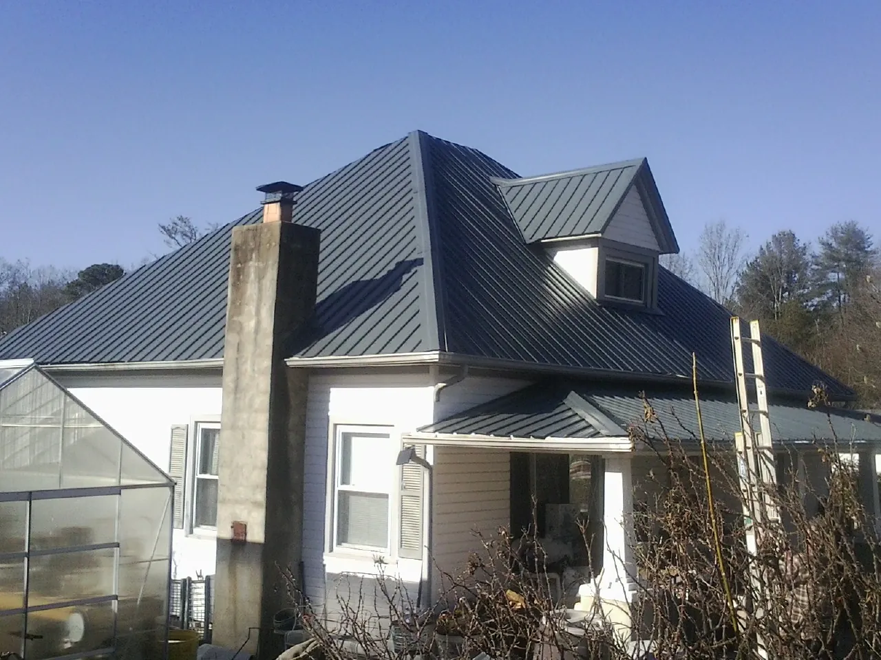 Dark blue standing seam metal roof on a white farmhouse with dormer — Slate & Tile Roof Repair by Roofing Brothers in Navarre