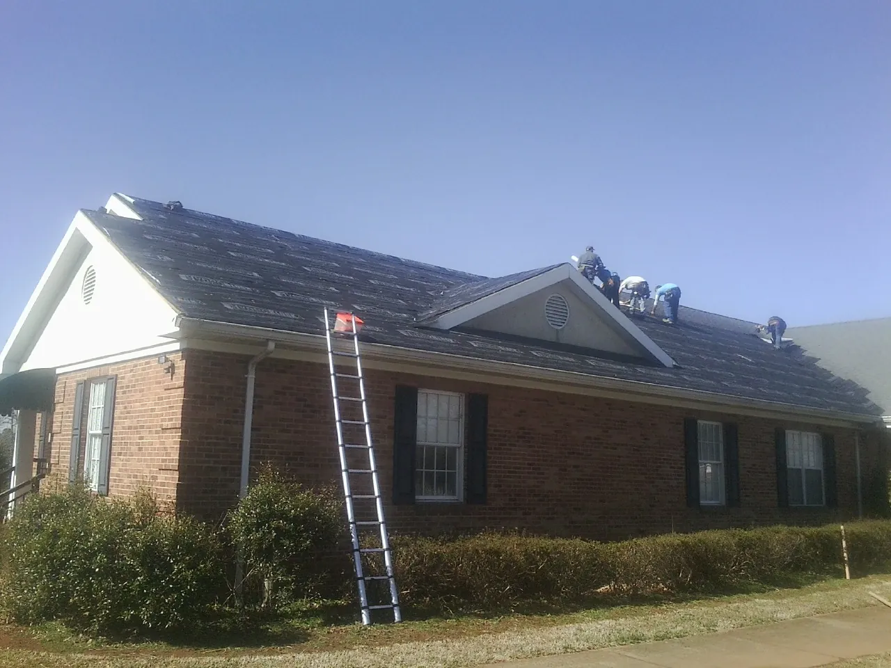 Crew tearing shingles off a brick ranch roof with a ladder set — Metal Roof Repair work by our crew in Navarre