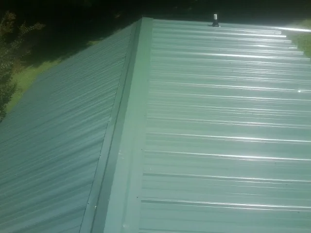 New green metal panels meeting at the ridge of a roof — Flat Roof Repair work by our crew in Navarre