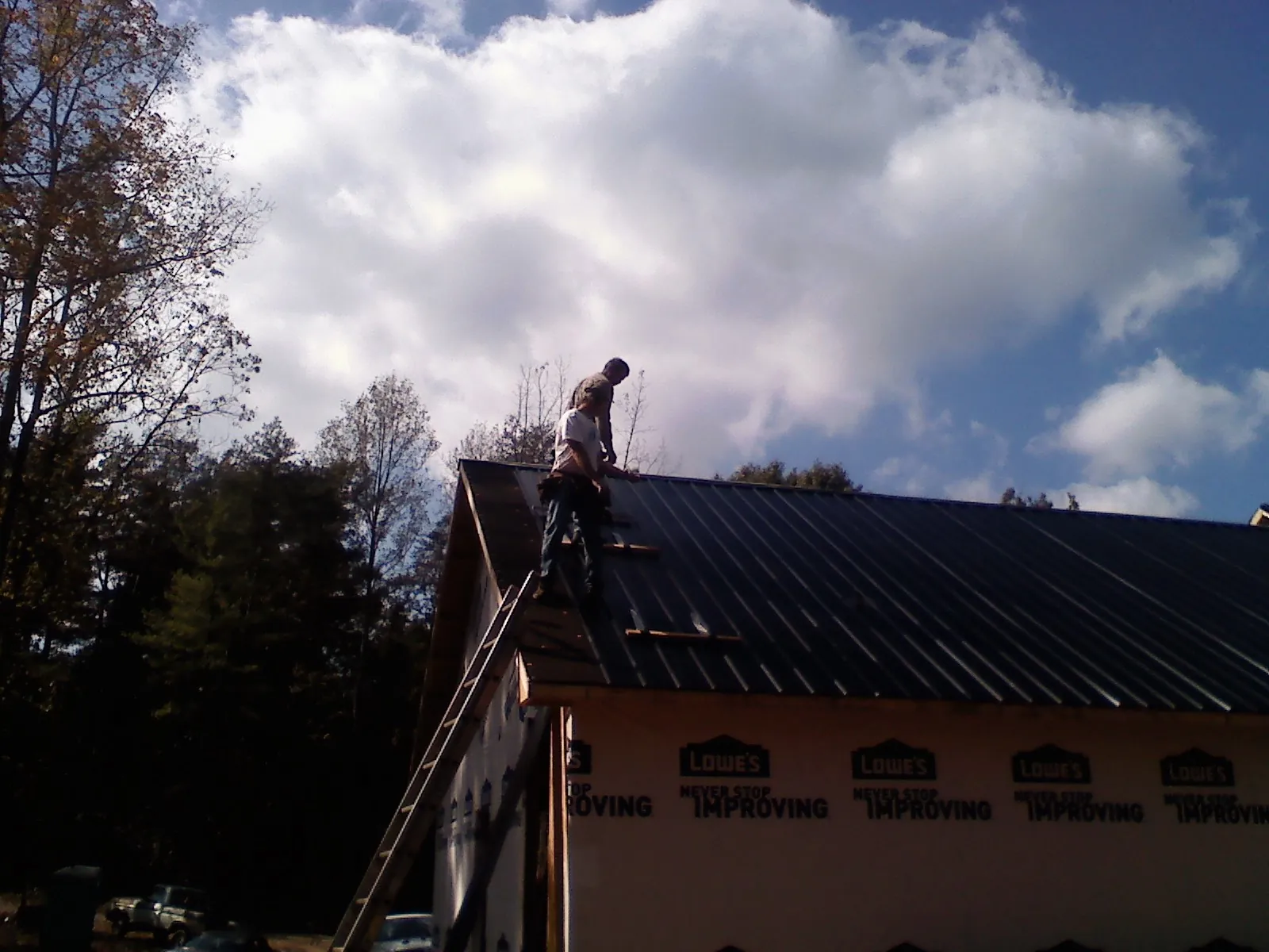 Roofer fastening dark metal panels high against a cloudy sky, from a Roof Inspection job in Navarre
