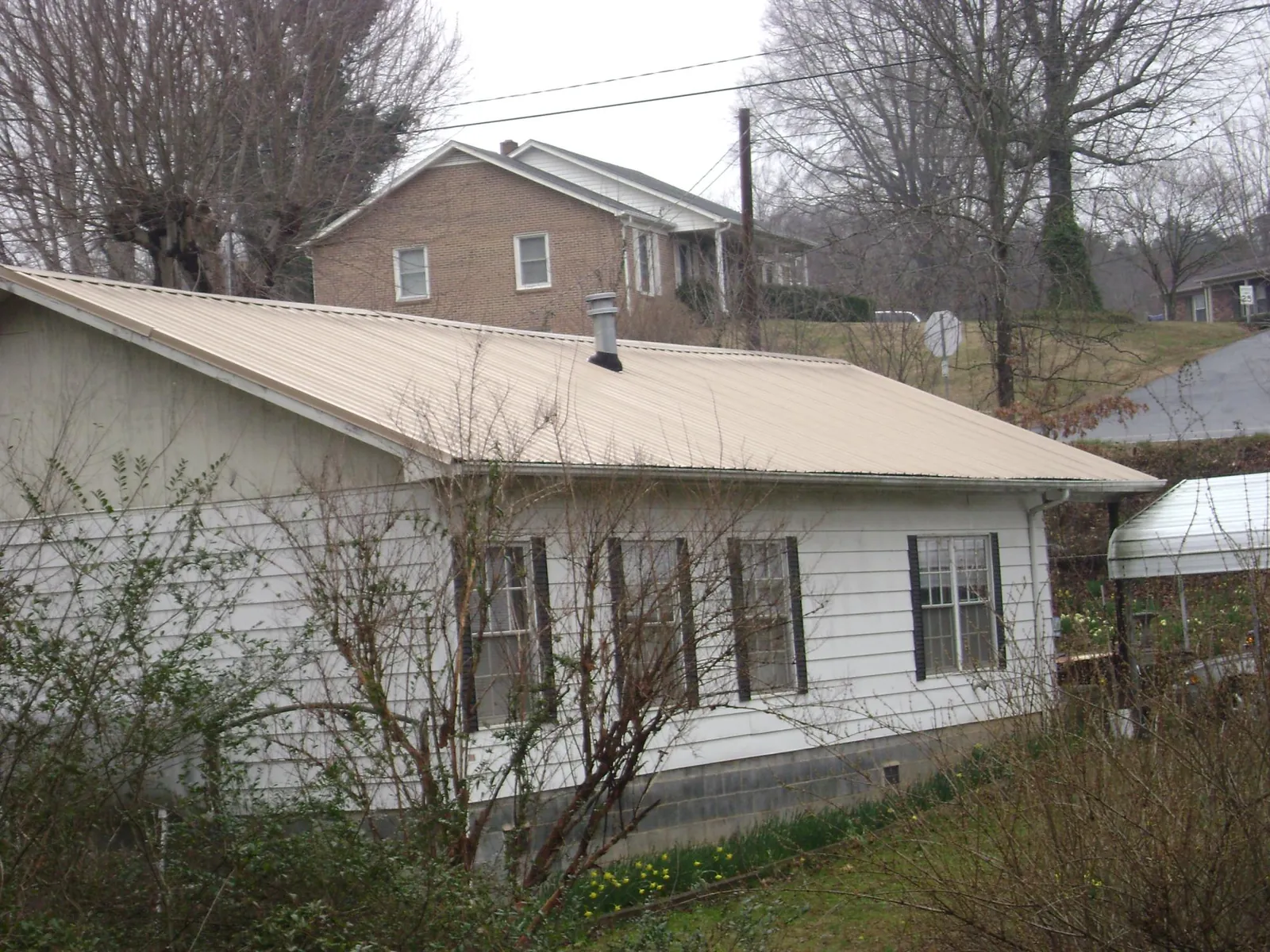 Tan metal roof on a white sided house set into a hillside — Commercial Roofing by Roofing Brothers in Navarre